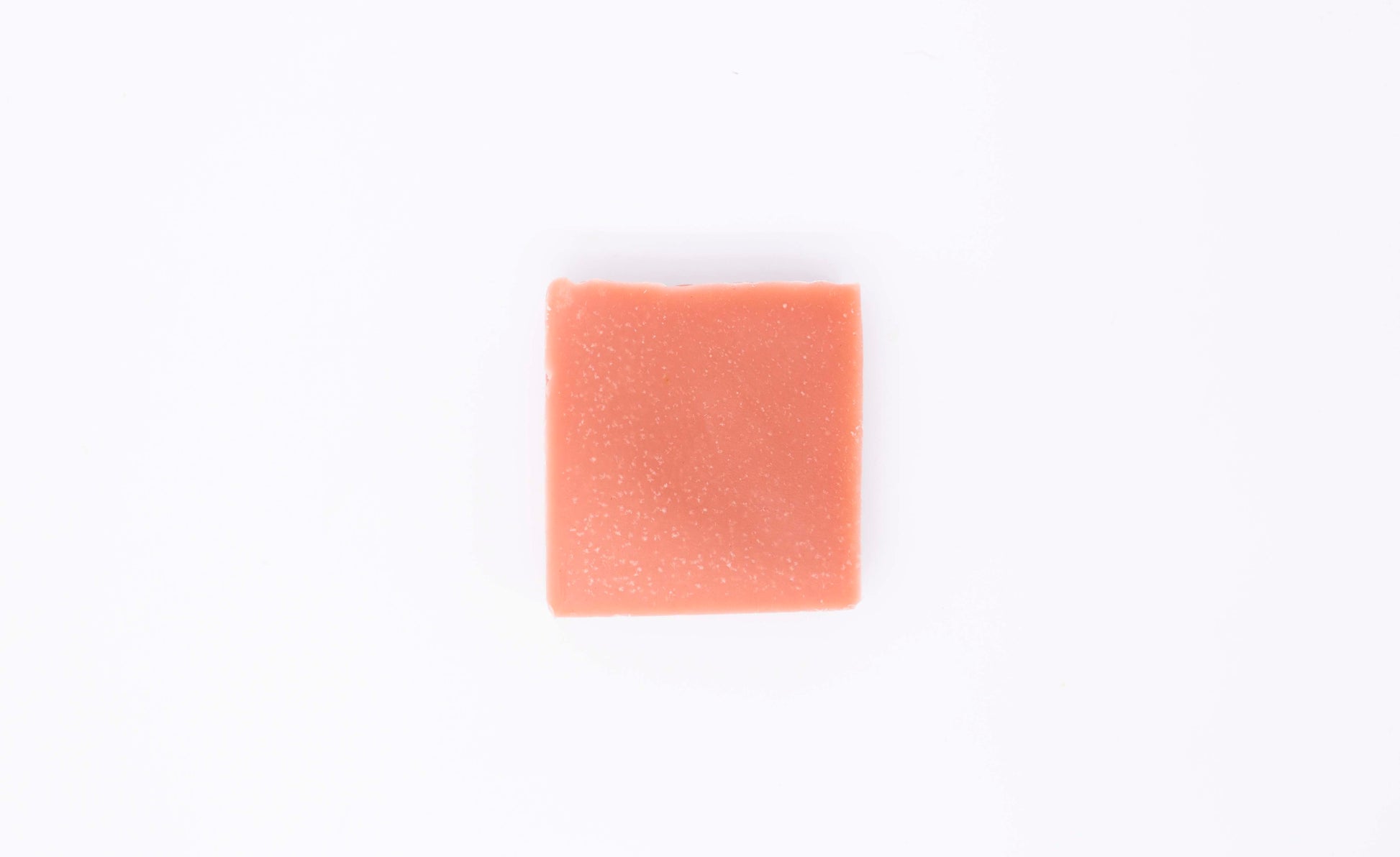 One vibrant coral peach colored geranium citrus soap bar sits on a clean white background