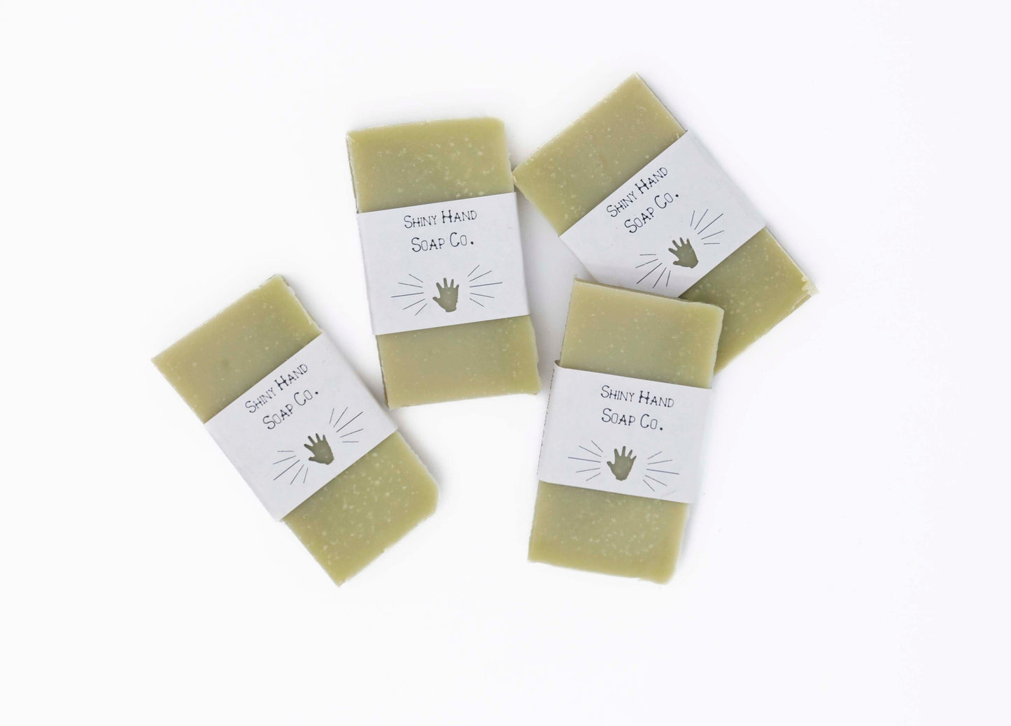 Four bright fresh vibrant green bergamot pine miniature soap bars sit on a clean white background with white paper wrappers that have a hand shape cut out of them.
