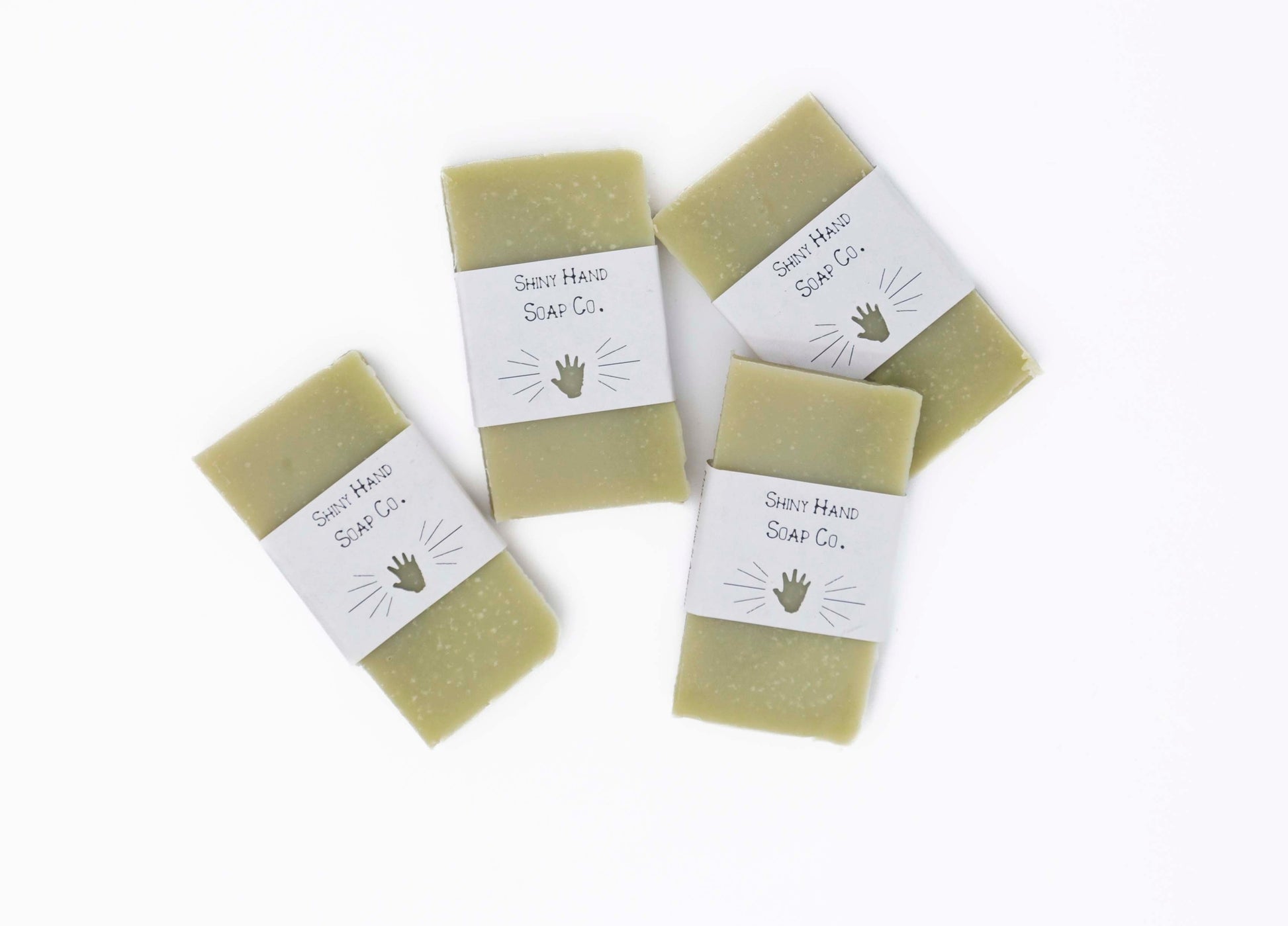 Four bright fresh vibrant green bergamot pine miniature soap bars sit on a clean white background with white paper wrappers that have a hand shape cut out of them.