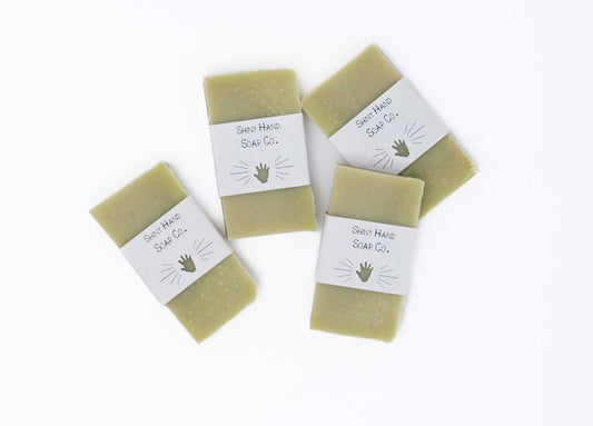 Four bright fresh vibrant green bergamot pine miniature soap bars sit on a clean white background with white paper wrappers that have a hand shape cut out of them.