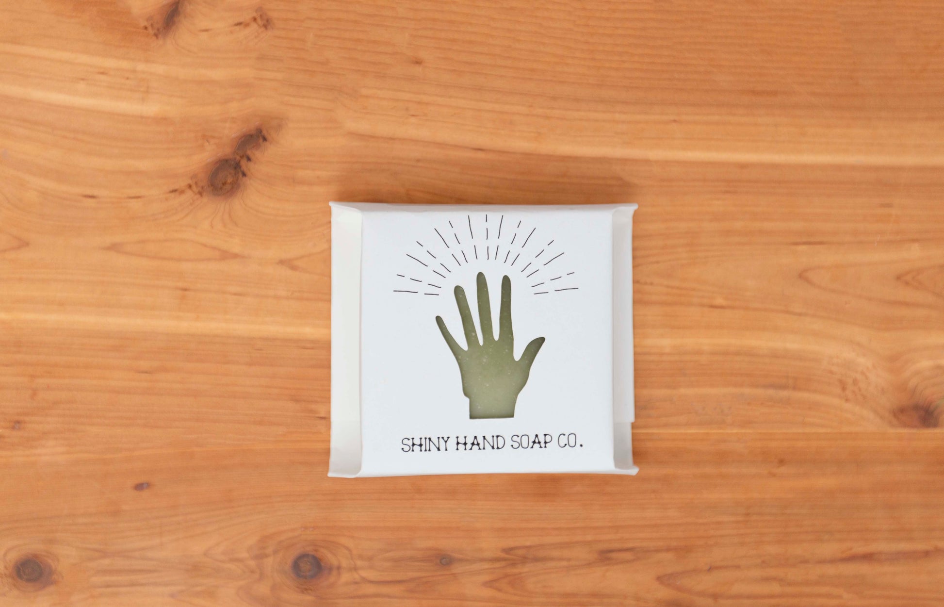 Four bright fresh vibrant green bergamot pine wrapped in a white recycled paper with a hand cutout shape against a wooden cedar background.