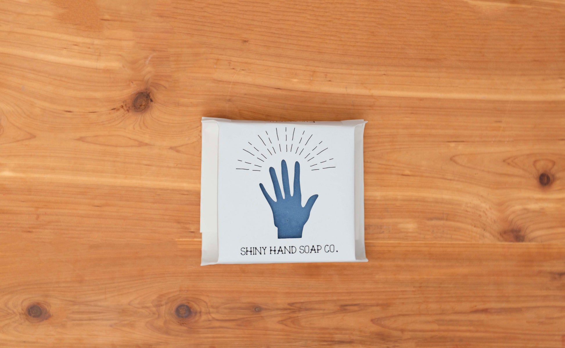 Royal cornflower blue eucalyptus soap bar  wrapped in a white recycled paper with a hand shaped cutout against a wooden cedar background.
