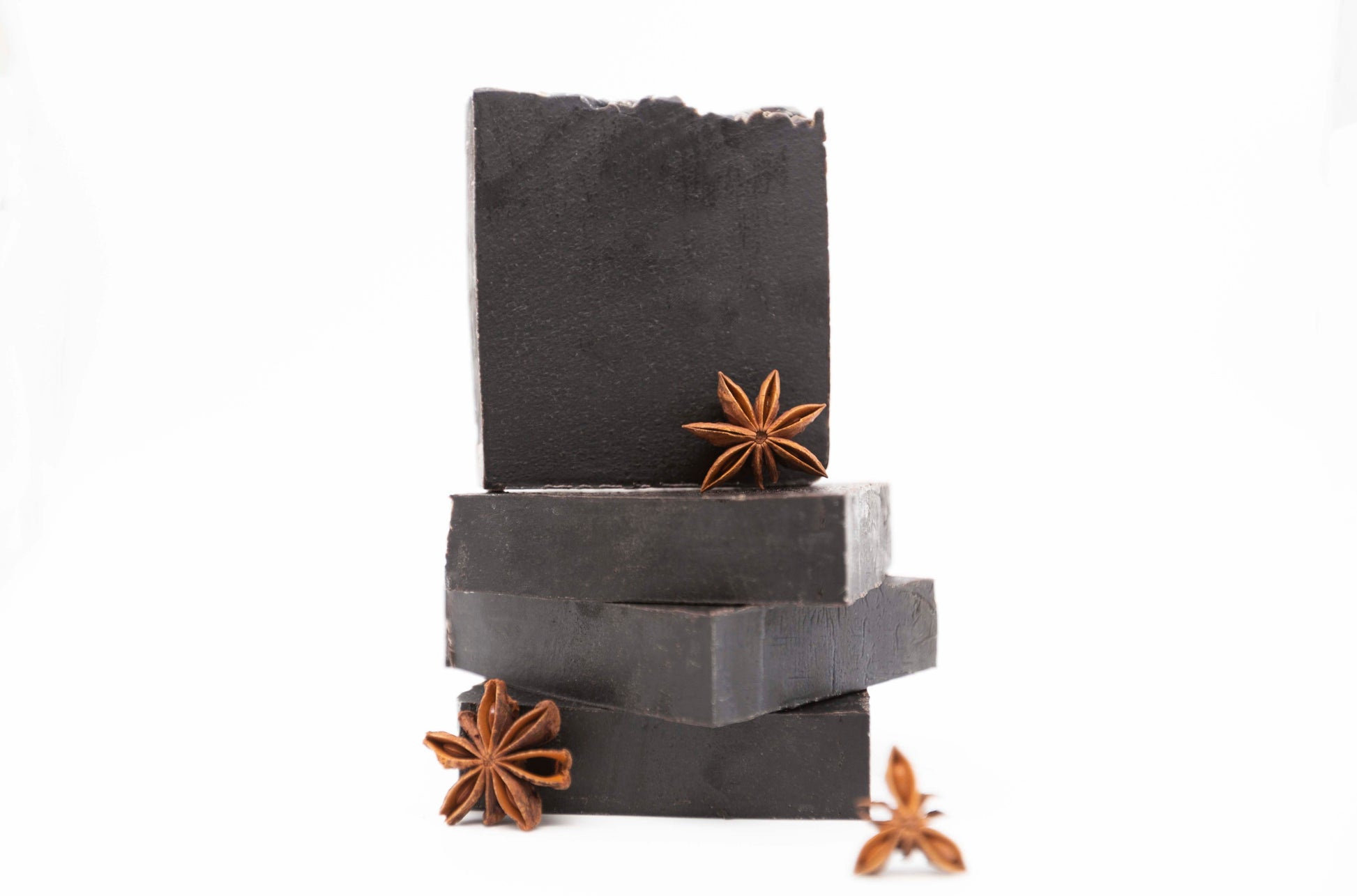 Four charcoal black Midnight Anise soap bars sit on a clean white background with brown fresh anise star pods