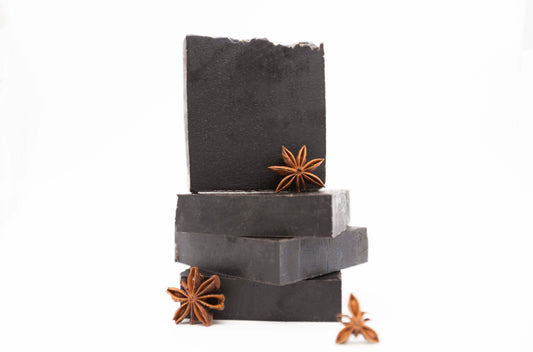 Four charcoal black Midnight Anise soap bars sit on a clean white background with brown fresh anise star pods