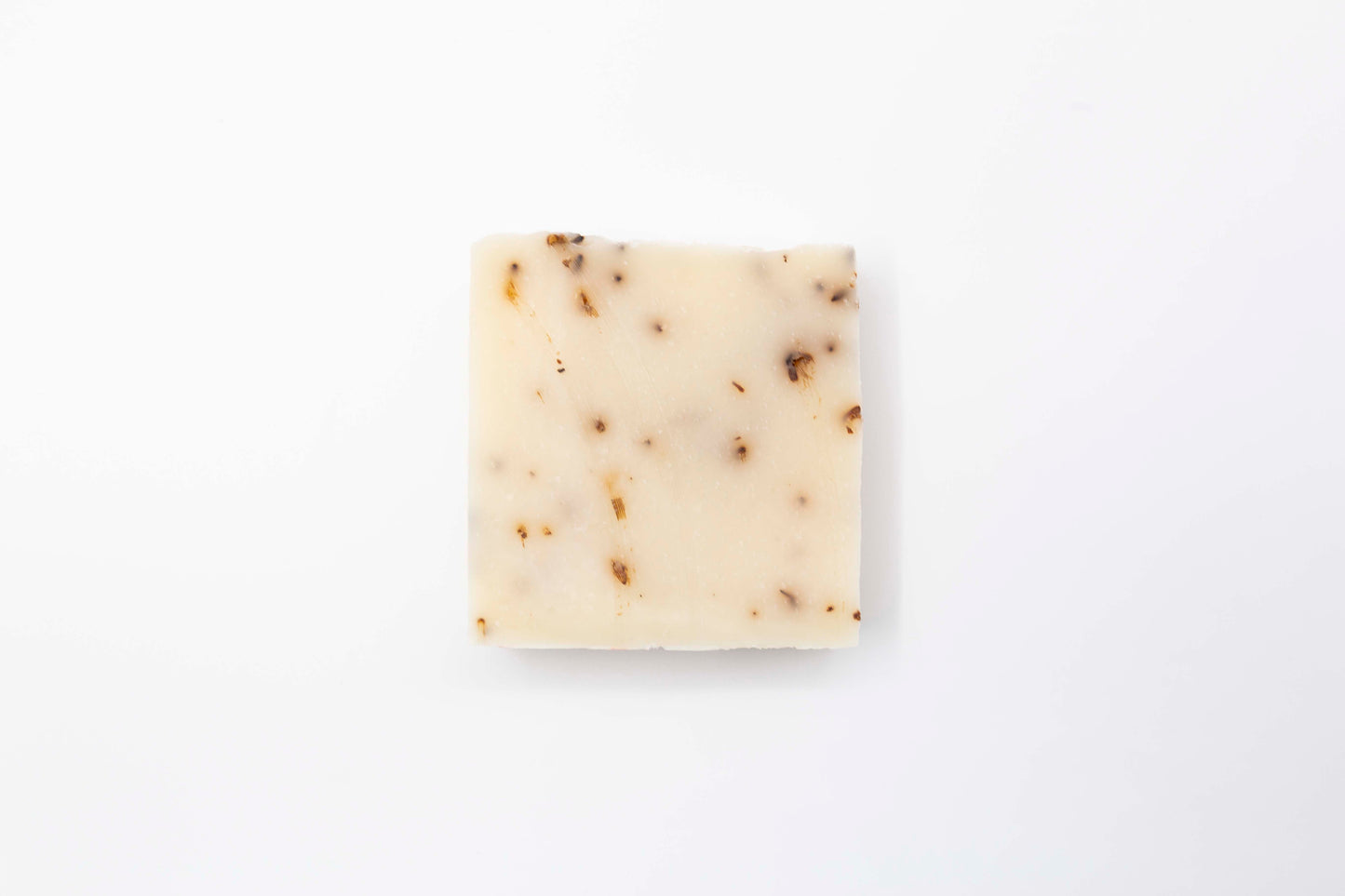 Ivory colored Lavender Blossom bar soap flecked with pale purple lavender flowers sits on a clean white background.