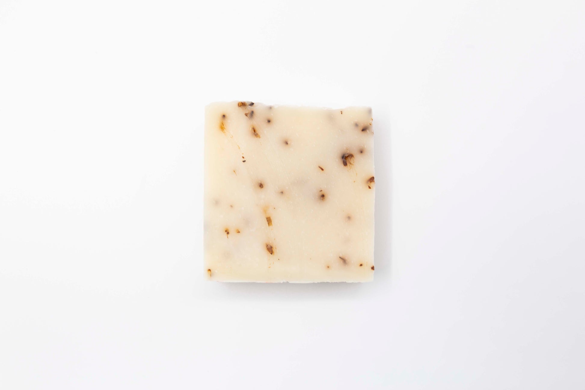 Ivory colored Lavender Blossom bar soap flecked with pale purple lavender flowers sits on a clean white background.