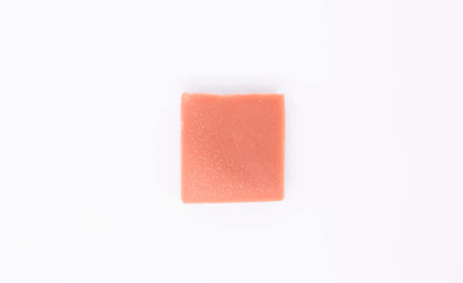 One vibrant coral peach colored geranium citrus soap bar sits on a clean white background