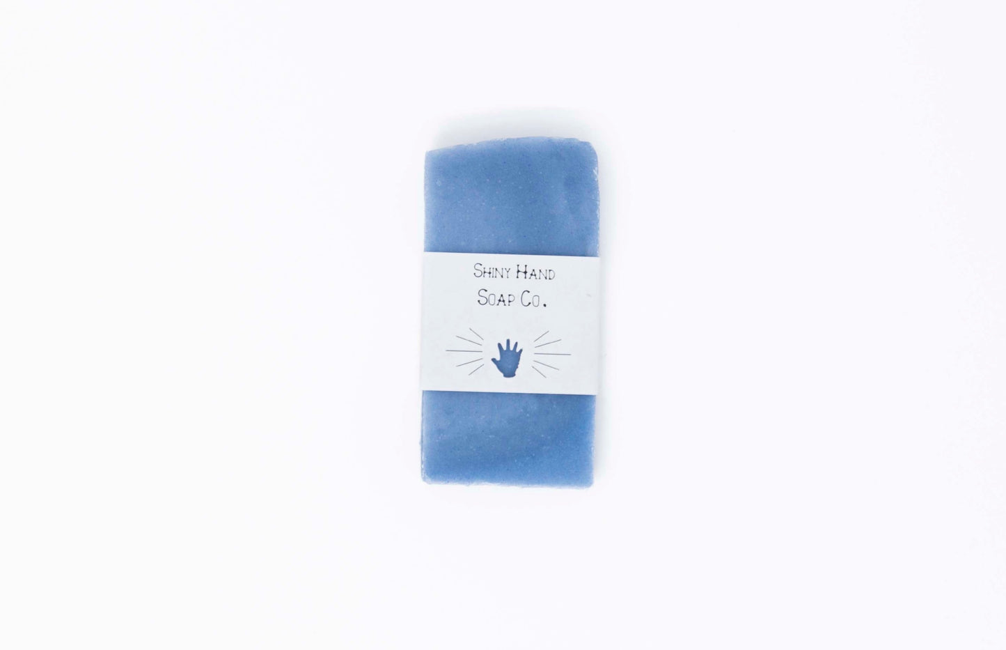 One bright royal blue miniature bar of eucalyptus lavender bar soap sits on a clean white background with a white paper wrapper that has a hand shape cut out of it.