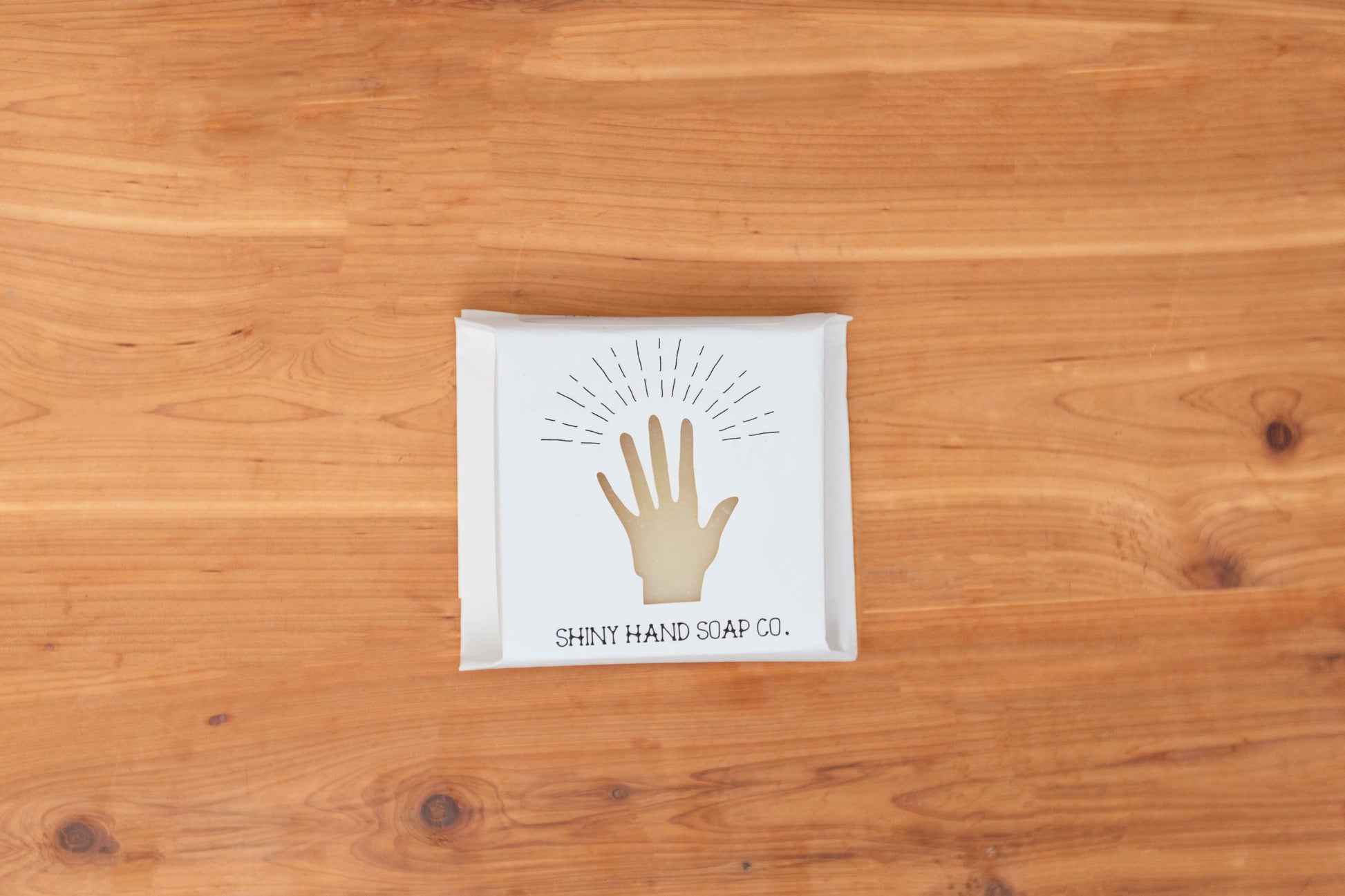 One creamy ivory white bar of Avocado Butter bar soap wrapped in a white recycled paper with a hand cutout shape against a wooden cedar background.