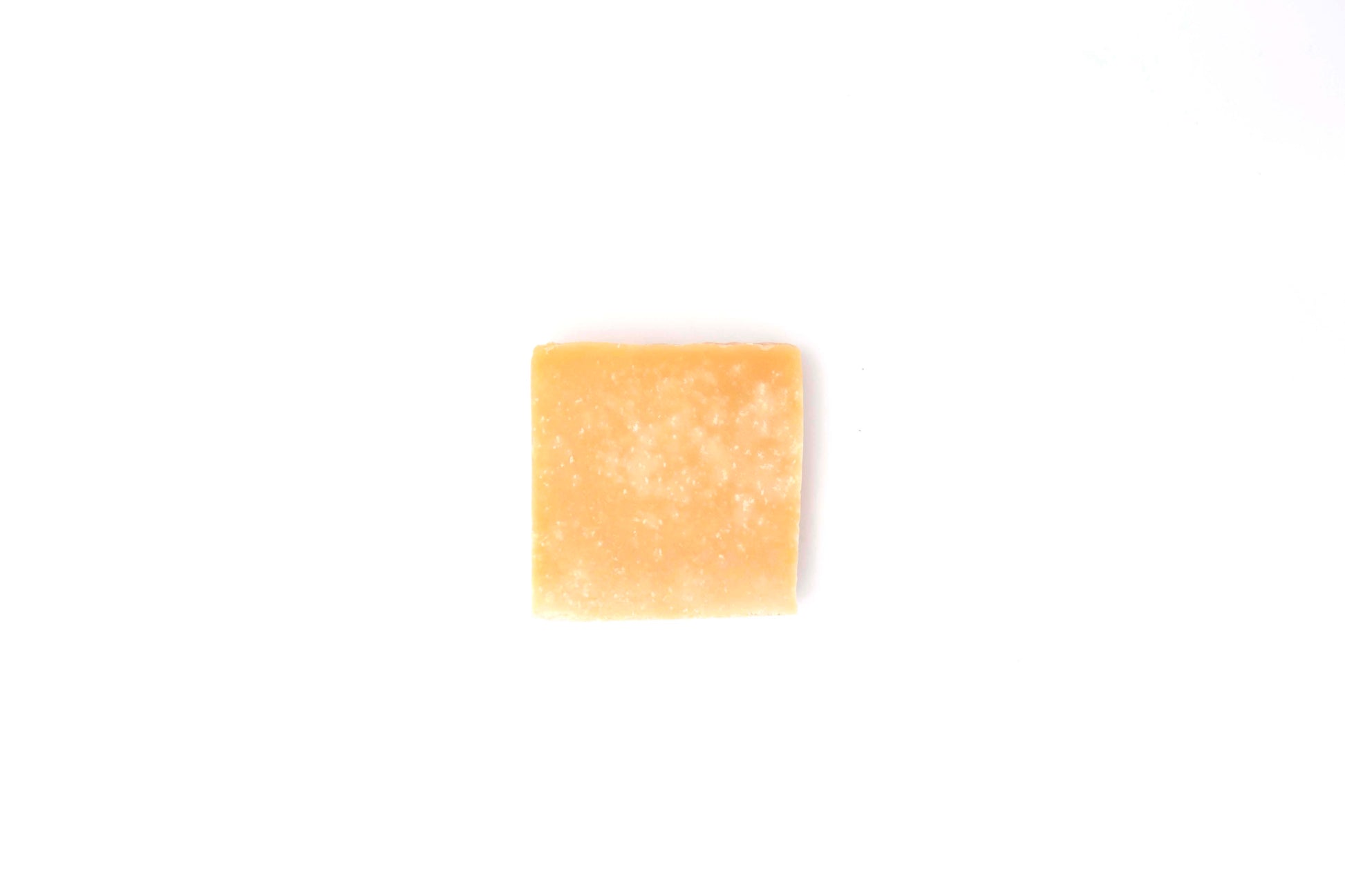 Rich yellow Lemon Sea Salt Soap bar flecked with white salt crystals rests on a clean white backdrop