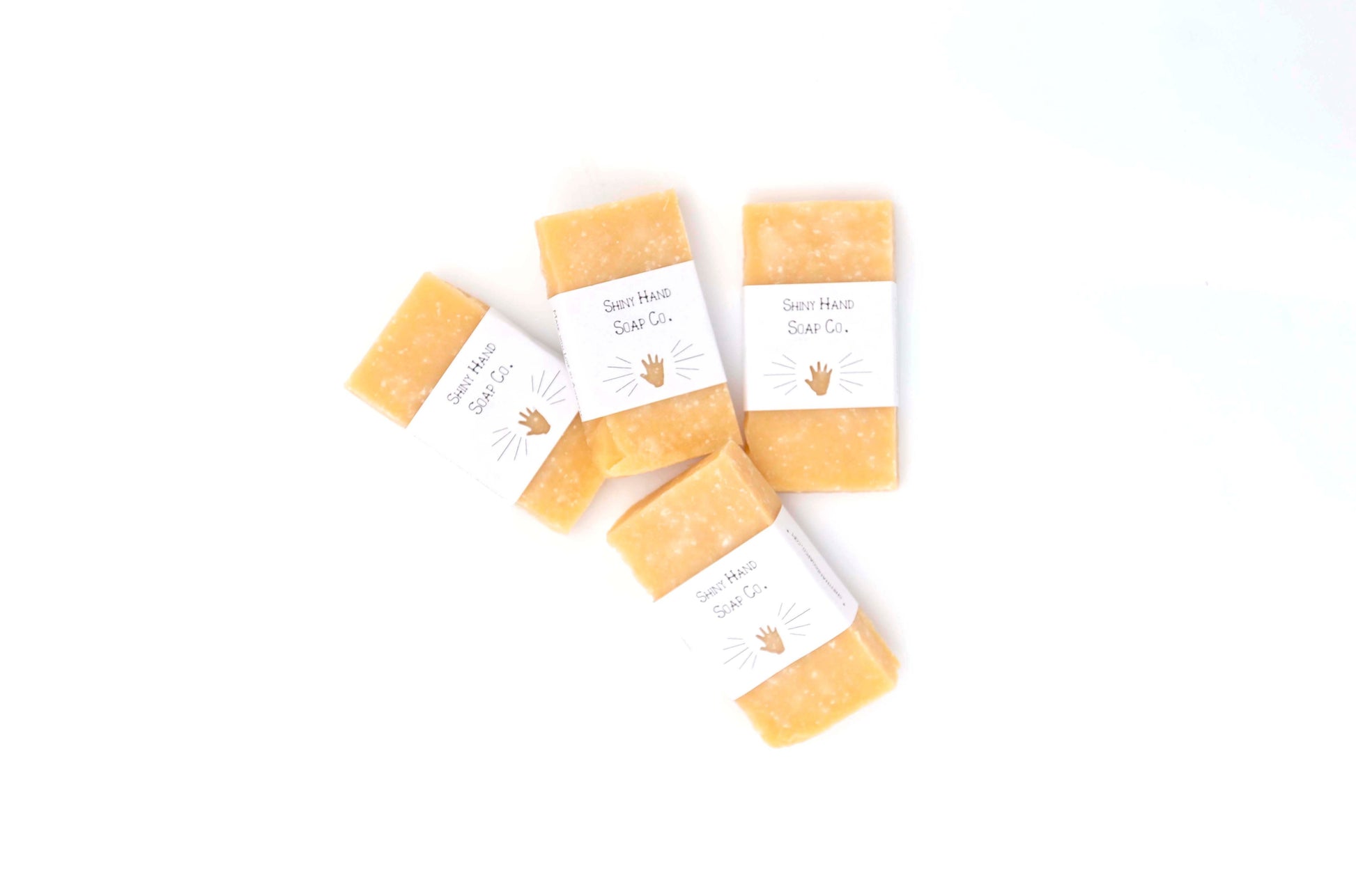 Four rich yellow Lemon Sea Salt Mini Sample Soaps flecked with white salt crystals sit on a clean white background in white recyled paper wrappers with a tiny hand cutout.