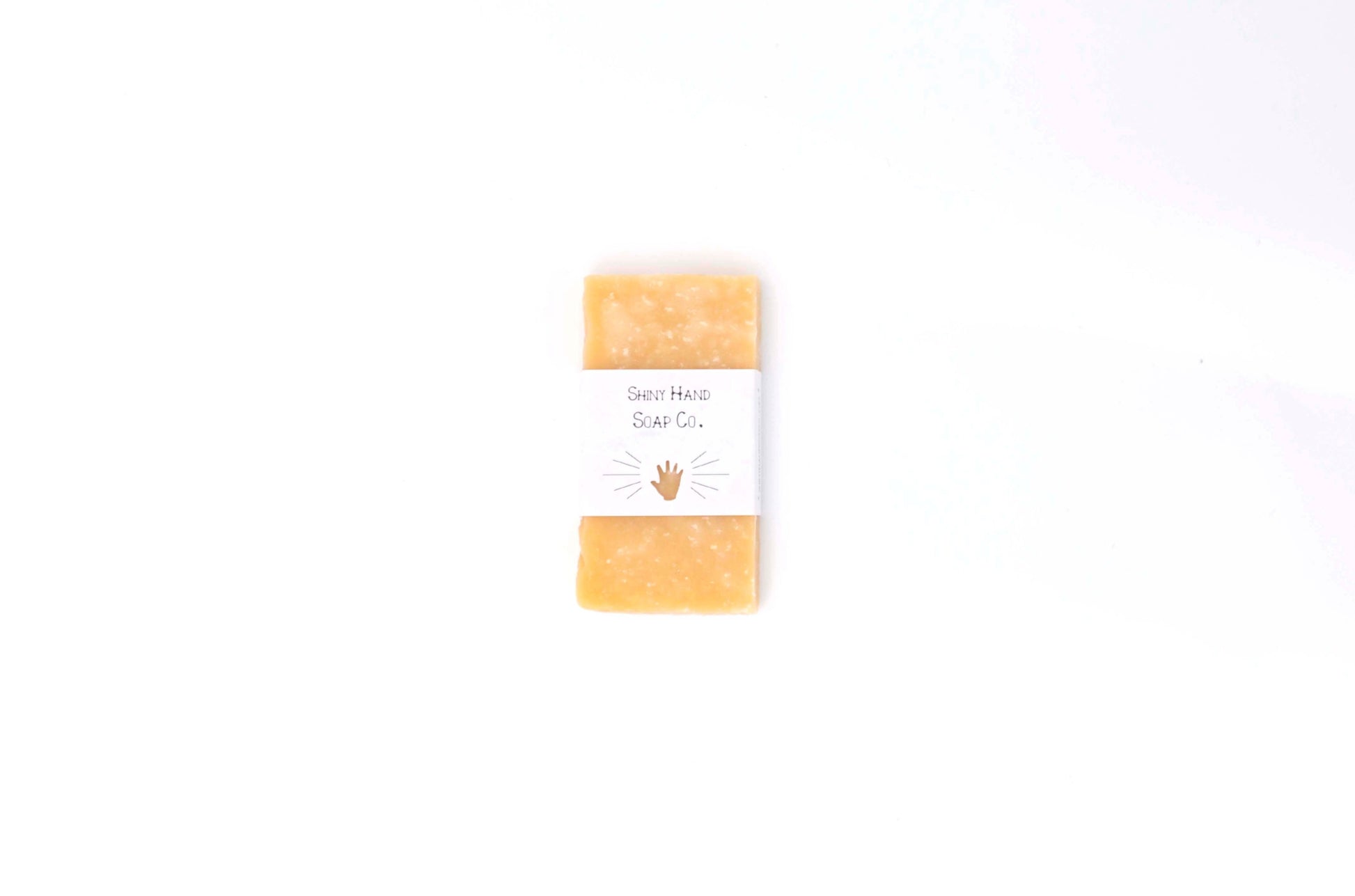 One rich yellow Lemon Sea Salt Mini Sample Soaps flecked with white salt crystals sits on a clean white background in white recyled paper wrapper with a tiny hand cutout.