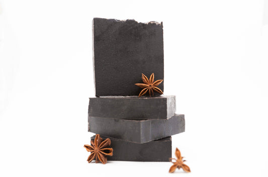 Four charcoal black Midnight Anise soap bars sit on a clean white background with brown fresh anise star pods 