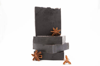 Four charcoal black Midnight Anise soap bars sit on a clean white background with brown fresh anise star pods 