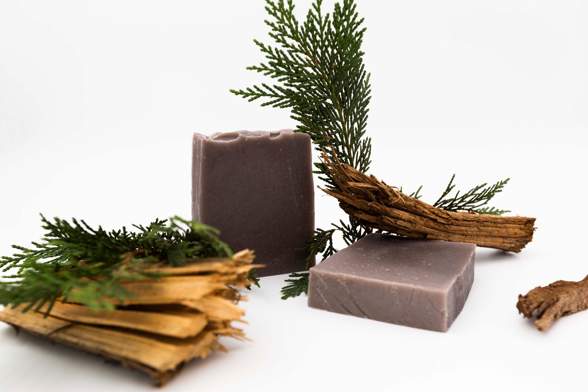 Brown Cedarwood patchouli soaps on a clean white backdrop with chunks of raw cedarwood and cedar leaf