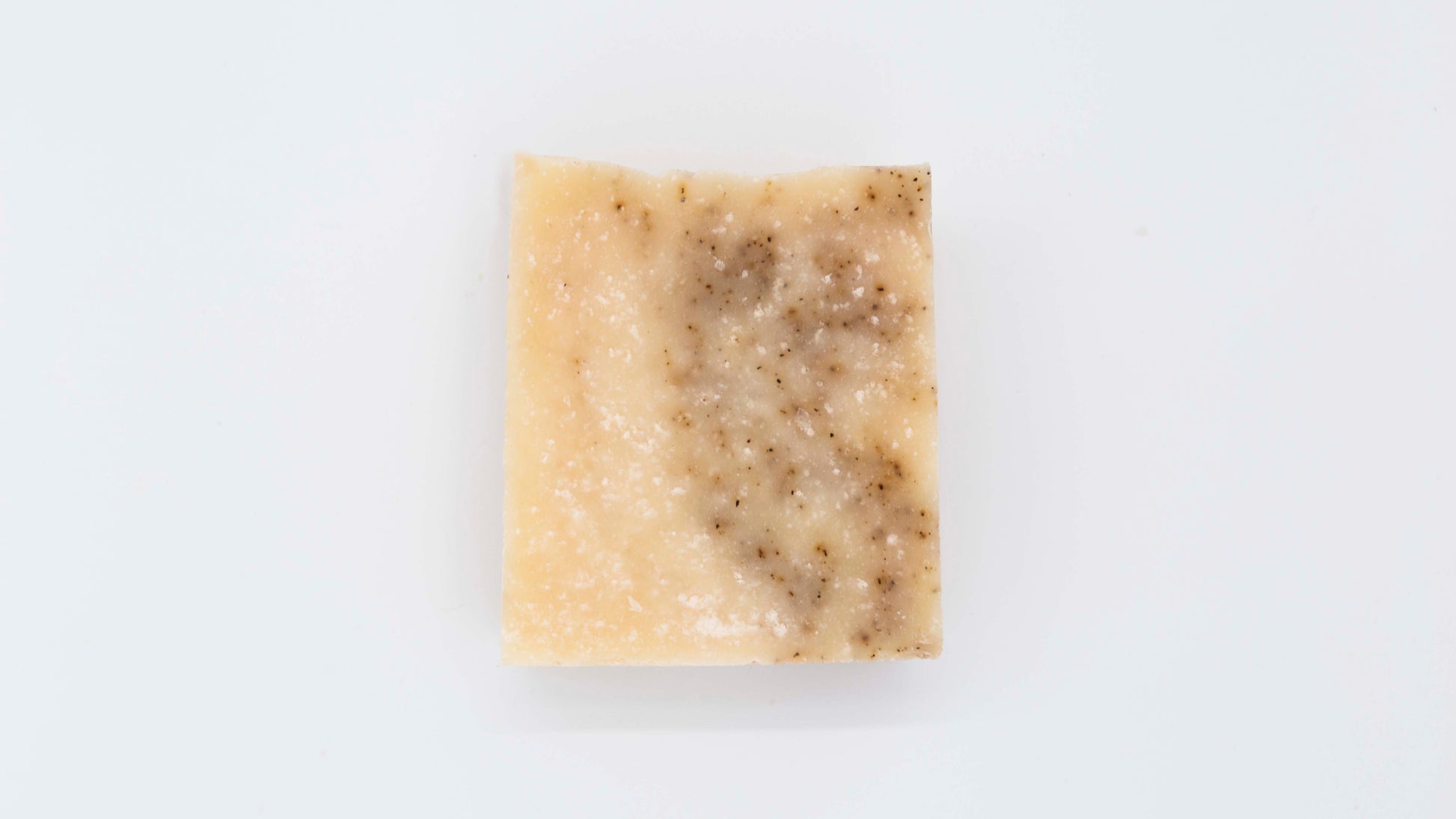 Ivory colored grapefruit black pepper soap bar with tiny specks of a black pepper swirl sits on a clean white background.