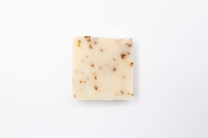 Ivory colored Lavender Blossom bar soap flecked with pale purple lavender flowers sits on a clean white background.